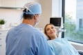 White male oral surgeon monitoring a calm patient during anesthesia in a modern oral surgery treatment room.