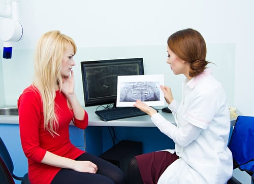 Closeup portrait female health care professional, dentist, holding showing panoramic dental X-ray, consulting woman patient having toothache.