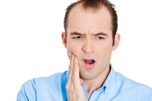 Closeup portrait of young man with sensitive tooth ache crown problem, suffering from pain, touching outside mouth with hand, isolated white background. Negative emotions, facial expression, feeling