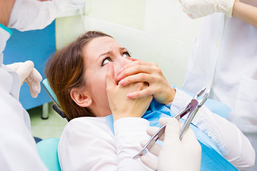 Closeup portrait young terrified girl woman scared at dentist visit, siting in chair, covering her mouth, doesn't want dental procedure, drilling, tooth extraction, isolated clinic office background