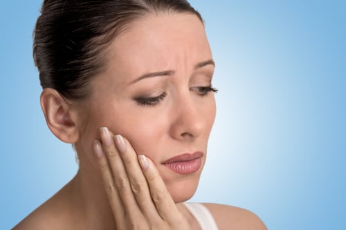 Closeup portrait young woman with sensitive tooth ache crown problem about to cry from pain touching outside mouth with hand isolated blue background. Negative emotion facial expression feeling