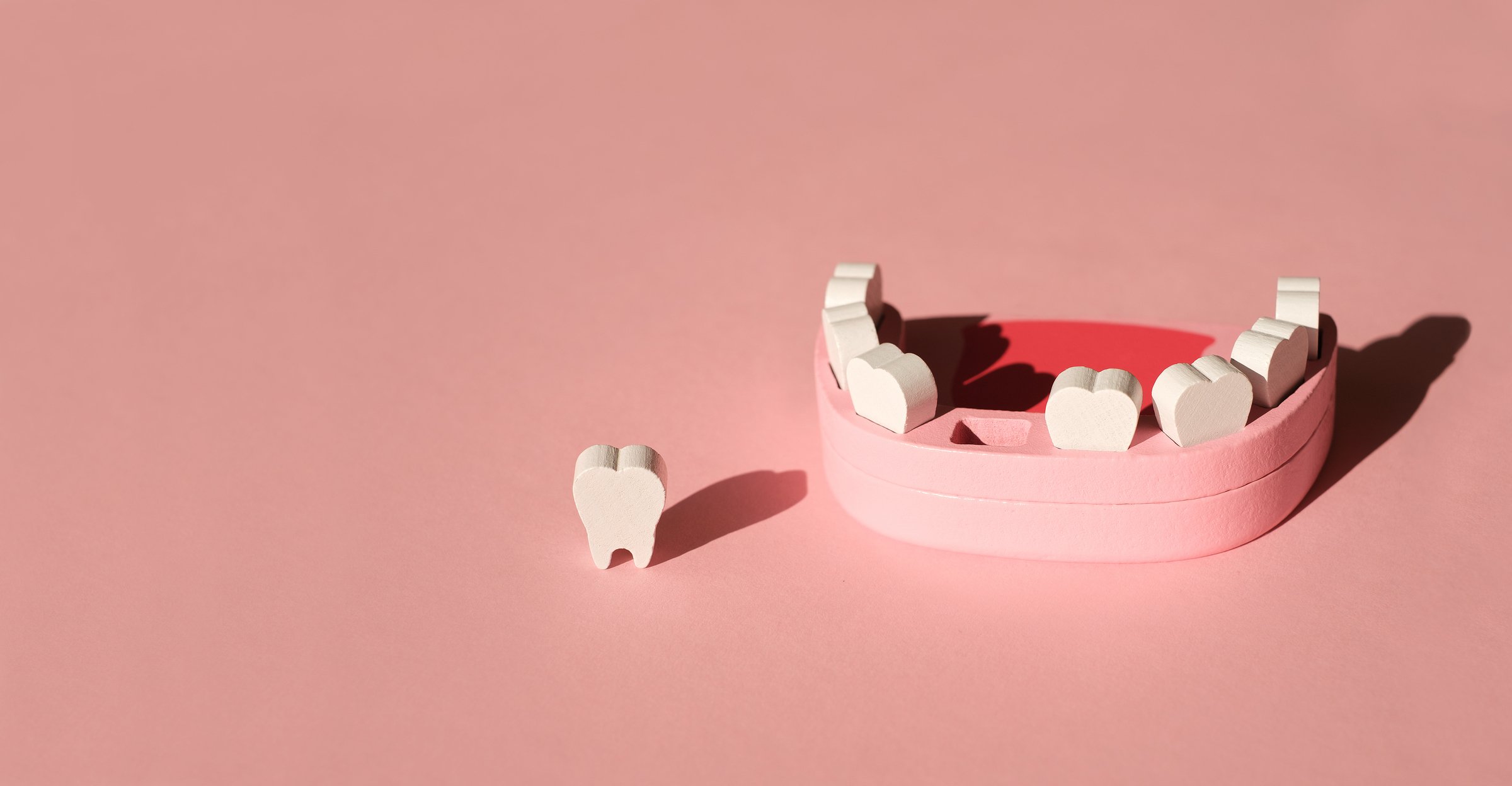 Wooden model toy of jaw with a missing tooth on pink background